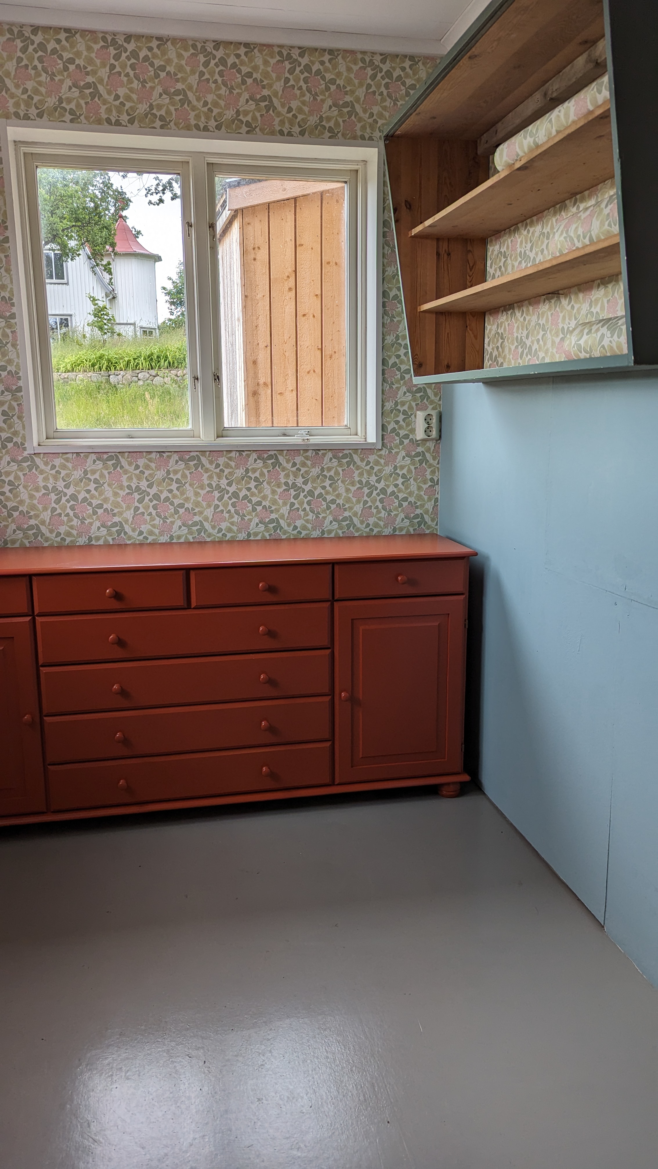 Nyrenoverat rum med småblommig tapet och röd byrå. 