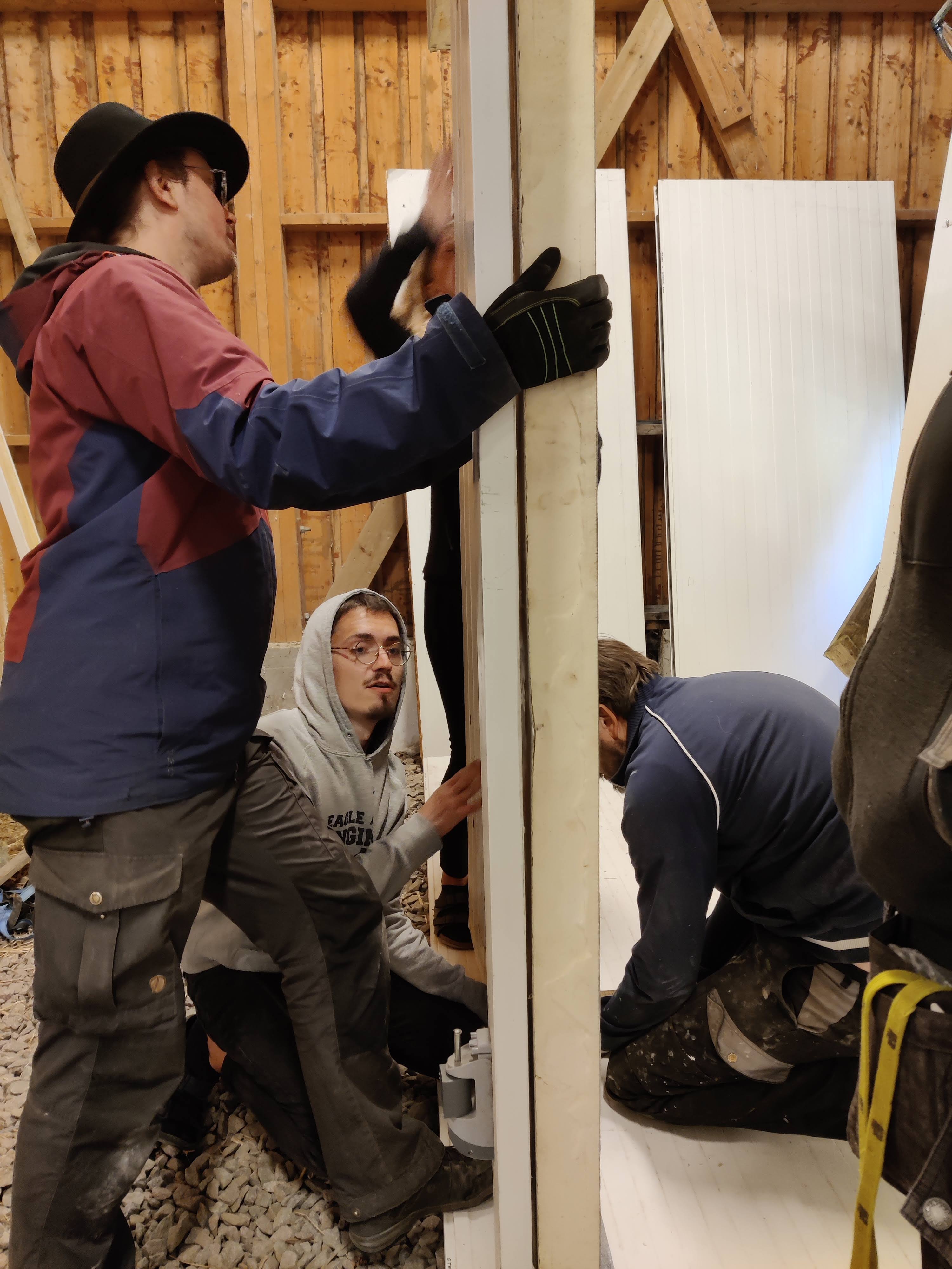 Flera personer håller i kylrumsvägg på väg att fästas.